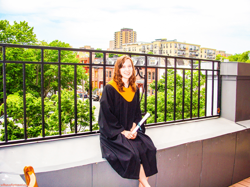 Jenn sitting on a ledge in a graduation gown with a diploma